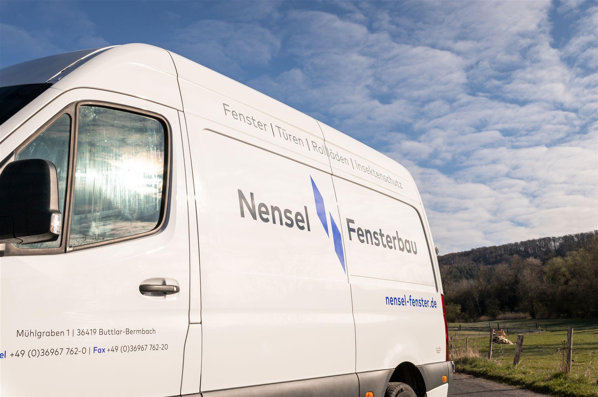 Seitenansicht eines weißen Firmenfahrzeugs mit der Aufschrift „Nensel Fensterbau“ und den Leistungen: Fenster, Türen, Rollläden, Insektenschutz.
