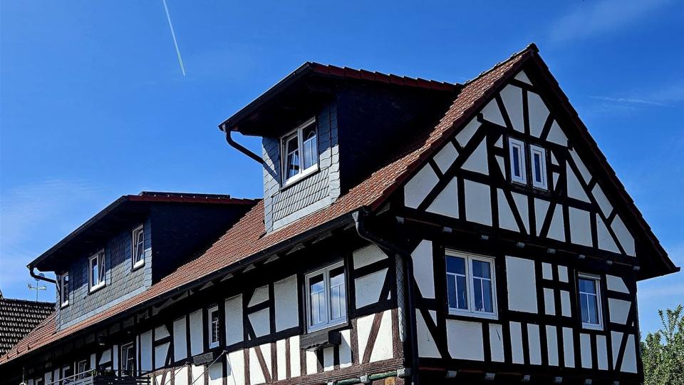 Das Bild zeigt ein renoviertes Fachwerkhaus mit weißer Fassade und dunklem Holzgebälk mit weißen Sprossenfenstern unter blauem Himmel.